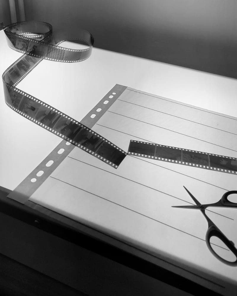 Bande de négatifs 35 mm posée sur une table lumineuse, à côté d'une pochette de rangement et d'une paire de ciseaux